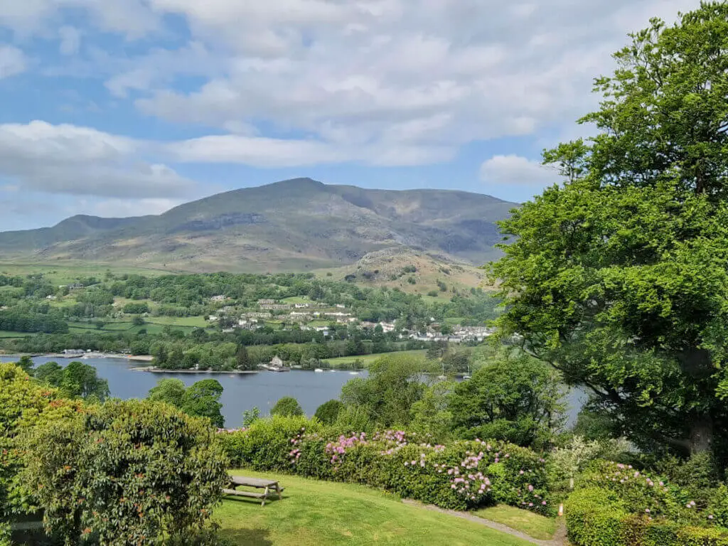 A view across a lake to a village of white houses. The sky is blue with clouds, there is a large lawn in the foreground
