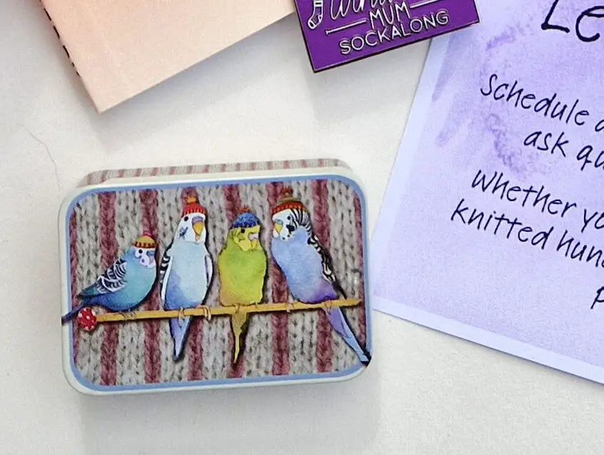 A close up of a small metal tin with a picture of budgies on it