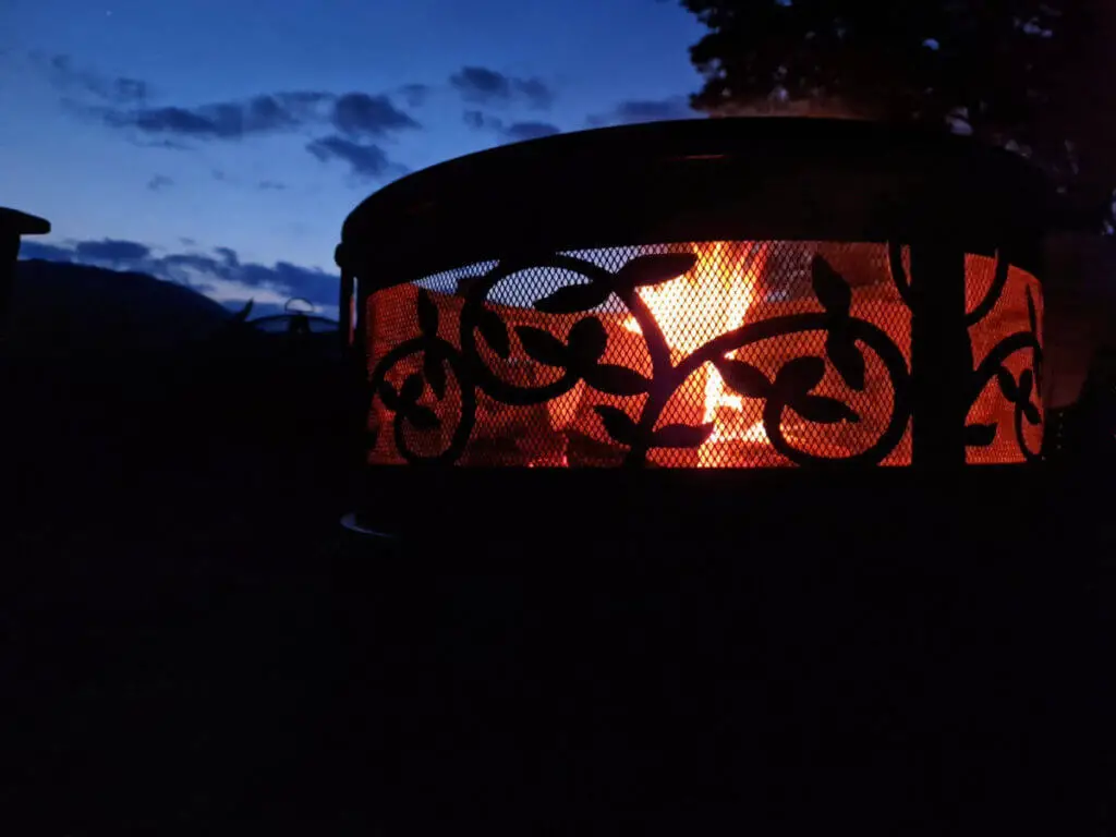 A close up of an ornamental fire pit against a dark sky. There is a fire inside the fire pit and it shows off the ornamental design