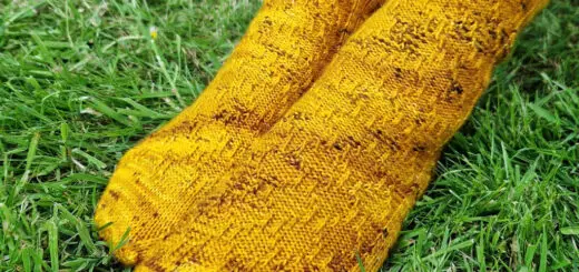 A pair of yellow twisted stitch socks modelled on feet, on the grass