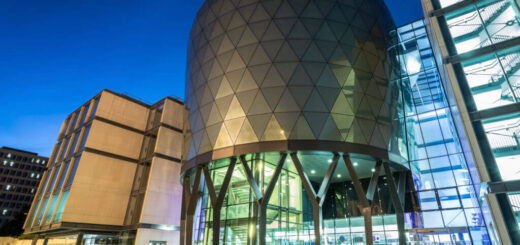 A futuristic-looking building with a round glass and silver-coloured tower between square ends is lit up against the night sky