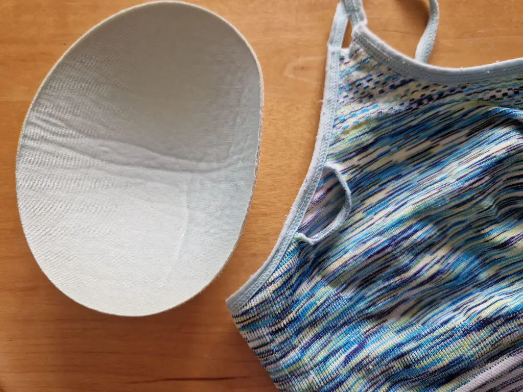 On the left, an egg-shaped padded shape which has come out of a small hole in a blue-patterned sports bra next to it