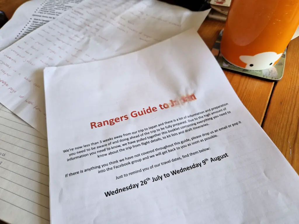 A paper document with "Rangers Guide to Japan" written in red ink across the front is lying on some other papers on a table.