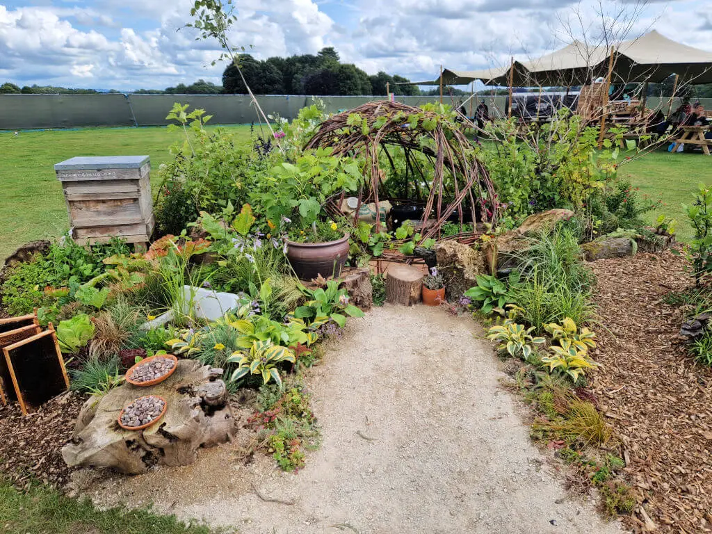 A willow dome stands at the end of a short gravel path, surrounded by plants chosen to attractor bees and other pollinators at RHS Tatton Show 2023