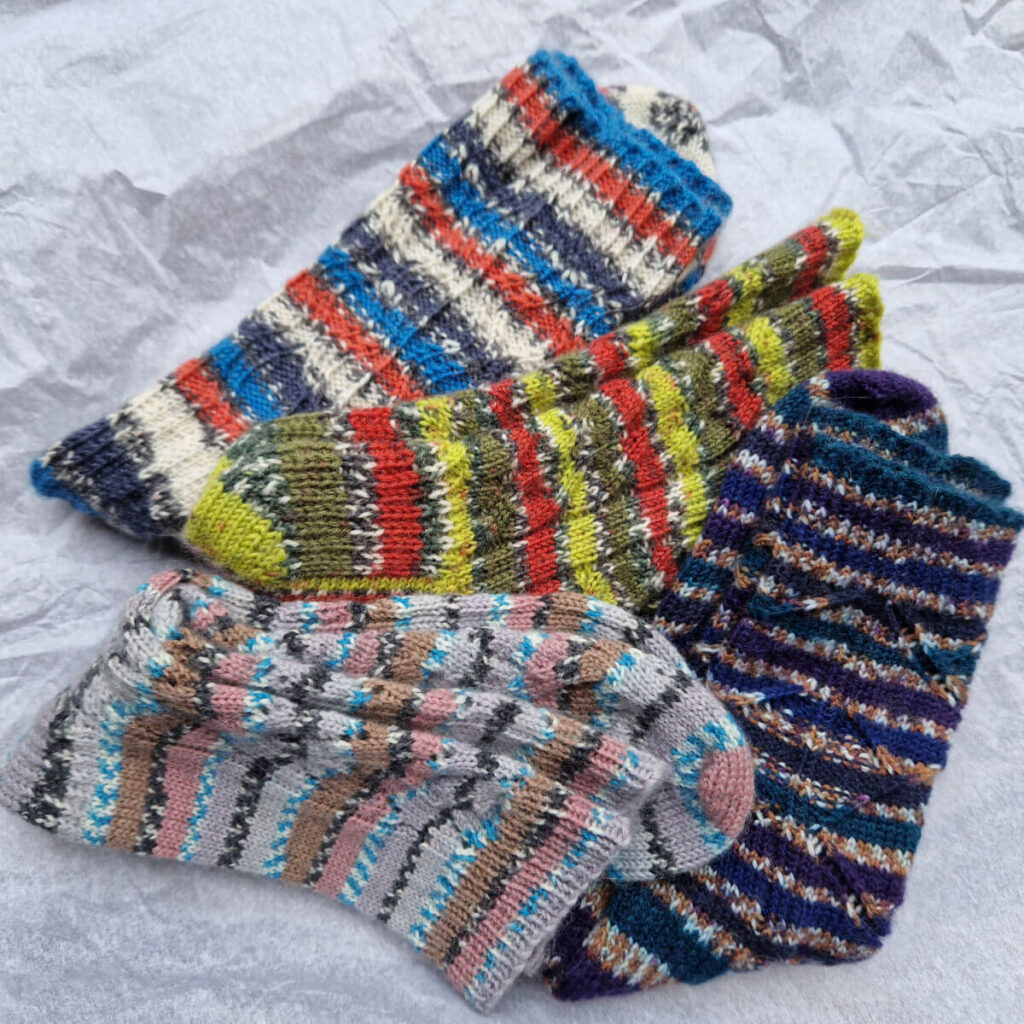Four pairs of striped socks lie together in a pile on a white tissue paper background