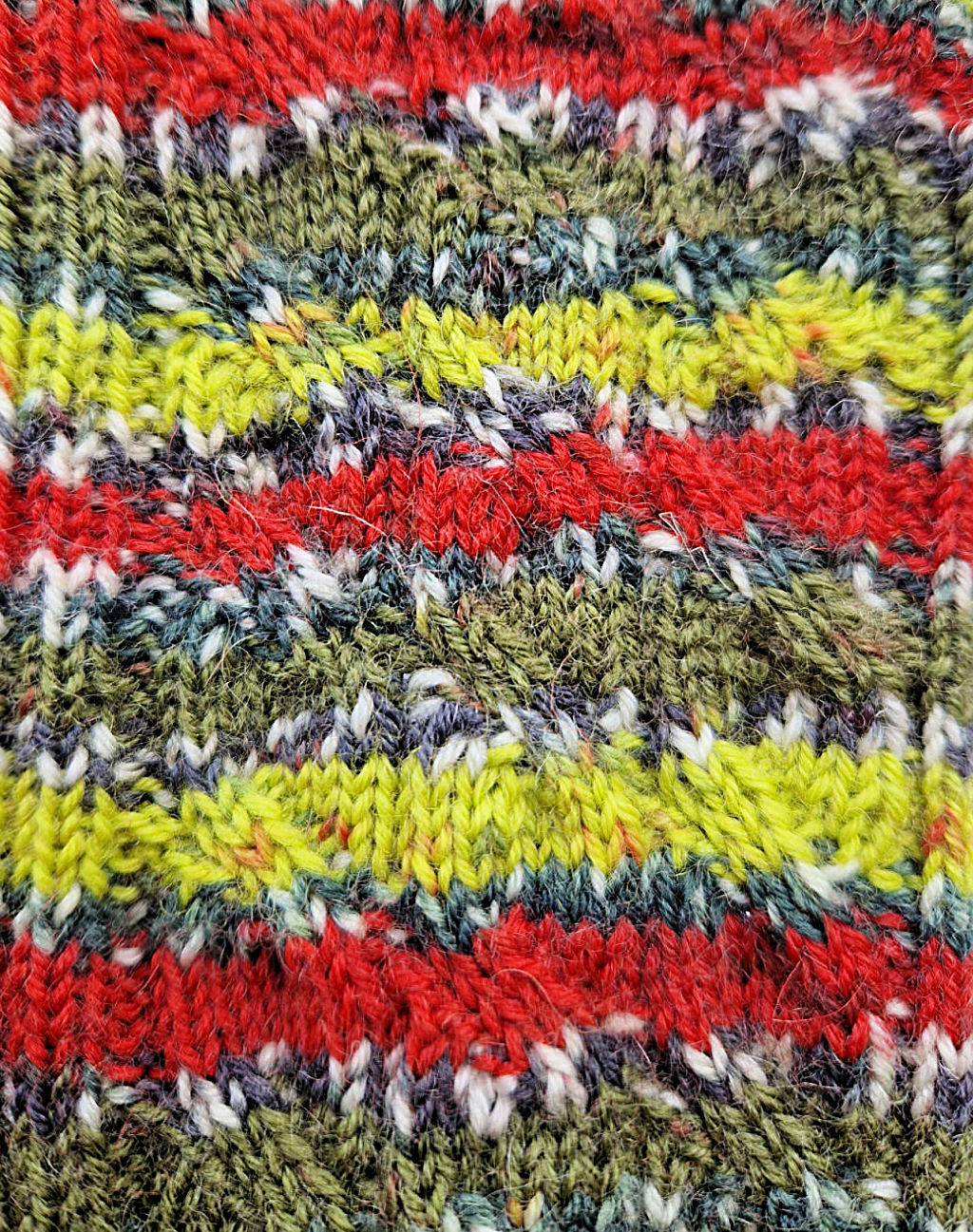 A close-up of the pattern on a pair of green, light green, red, black and white socks. 