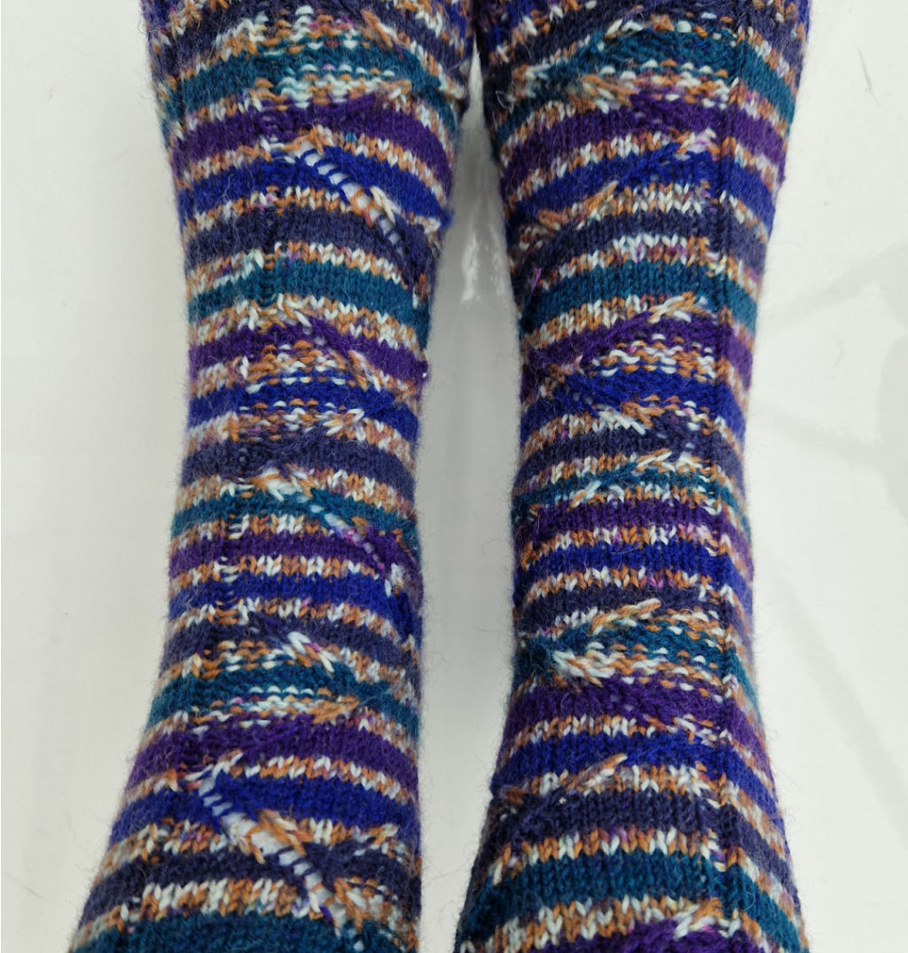 A close-up of the pattern on a pair of navy, teal, purple, gold and white socks. 