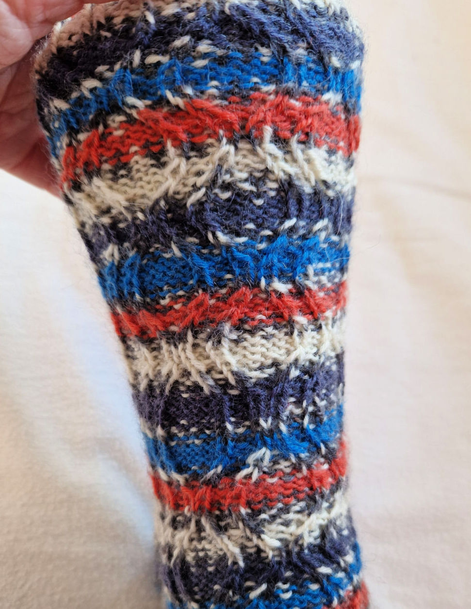 A close up of a twisted stitch hourglass pattern on a striped sock