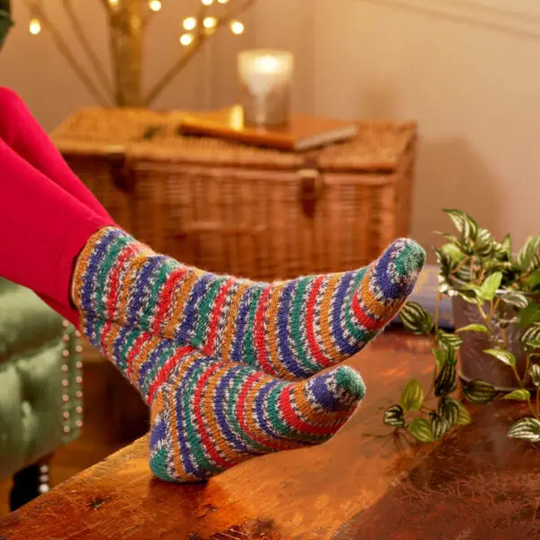 A pair of feet resting on a wooden coffee table, wearing hand knitted socks in stripes of blue, green, red and gold