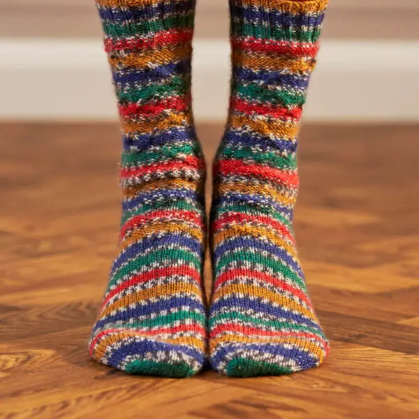 The front view of a pair of feet wearing hand knitted socks in stripes of blue, green, red and gold