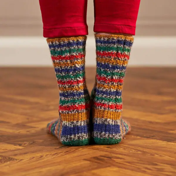 The back view of a pair of feet wearing hand knitted socks in stripes of blue, green, red and gold