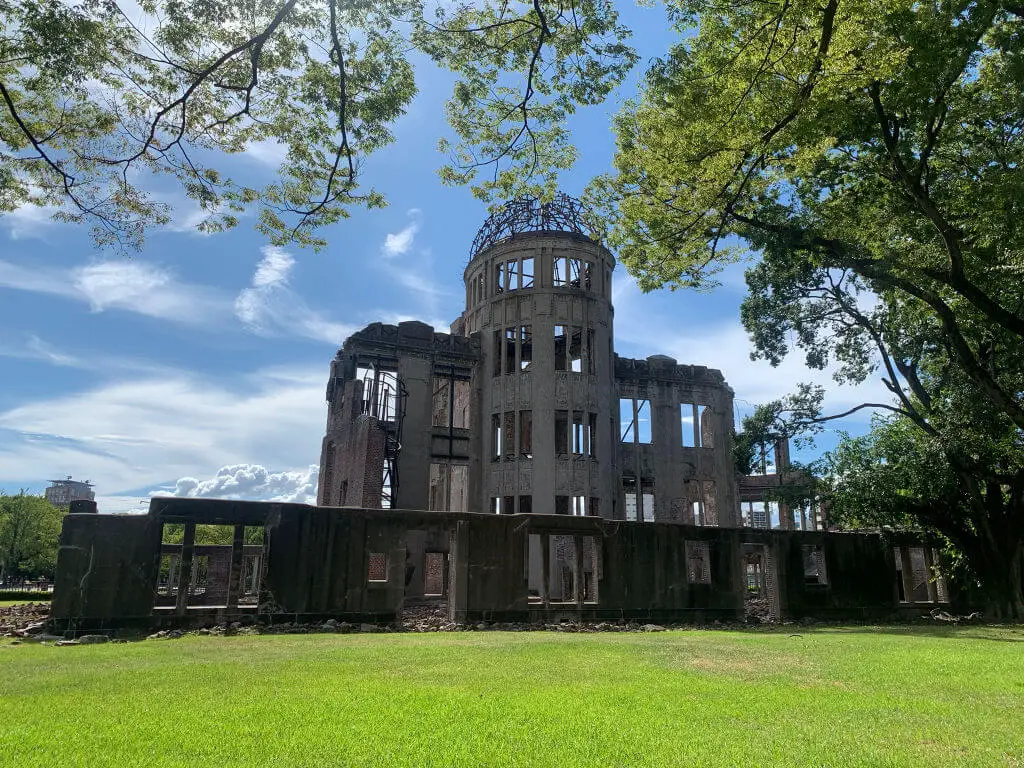 The shell of Hiroshama bomb dome framed by trees and grass against a blue sky