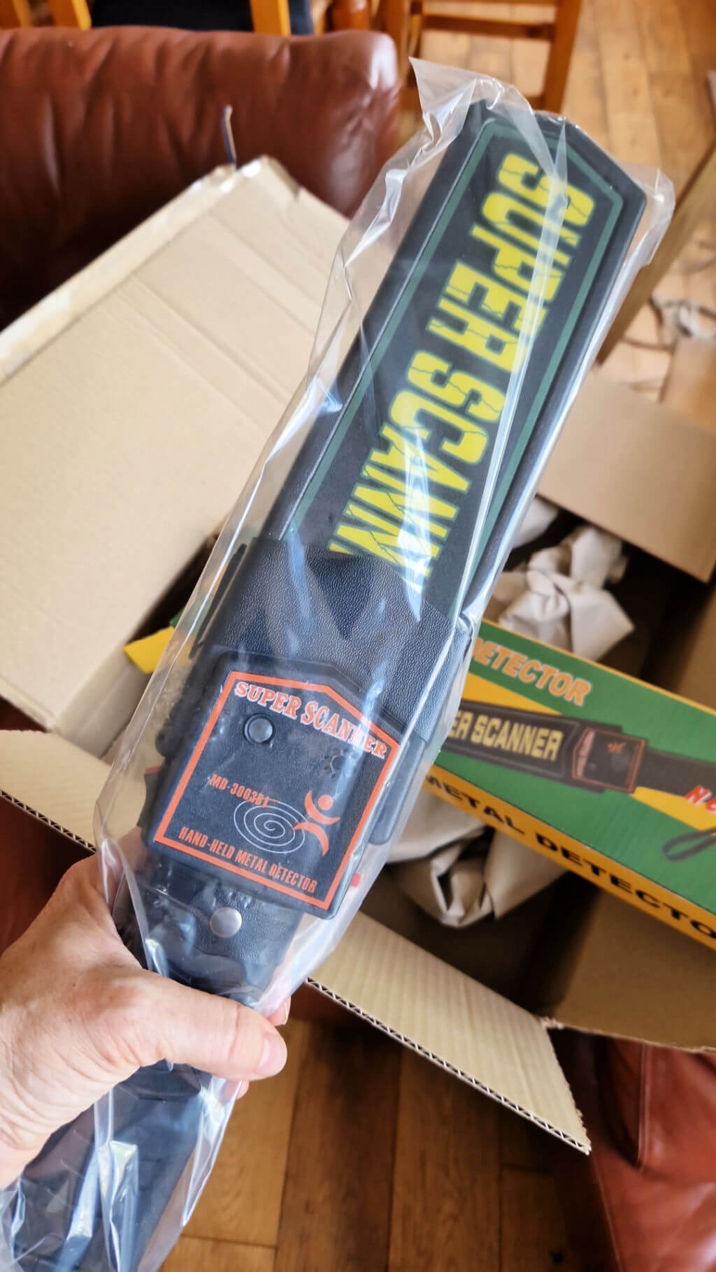 A large hand-held metal detector held over a cardboard box for scale