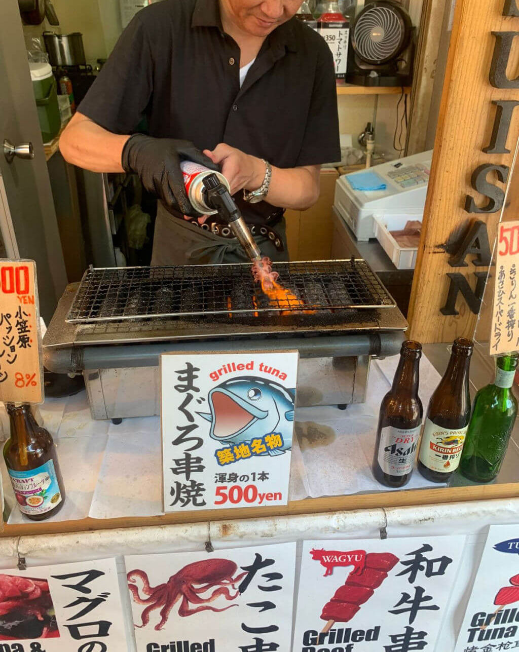 A man is using a blow torch to cook seafood at an outdoor food stall
