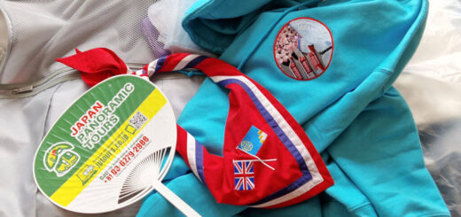 An open suitcase with a turquoise blue hoody, a red, blue and white Guide necker (neckerchief) and a green and yellow fan lying on it