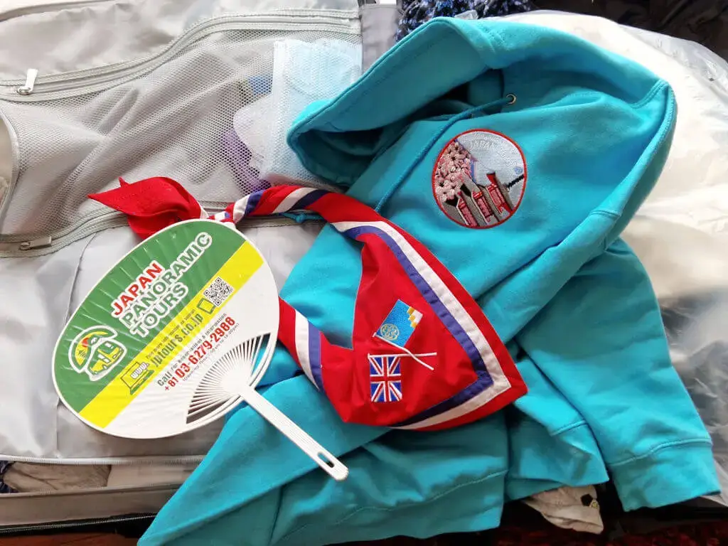 An open suitcase with a turquoise blue hoody, a red, blue and white Guide necker (neckerchief) and a green and yellow fan lying on it