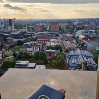 A view across Manchester from the cocktail bar of a tall hotel building. There is a cocktail menu on the table