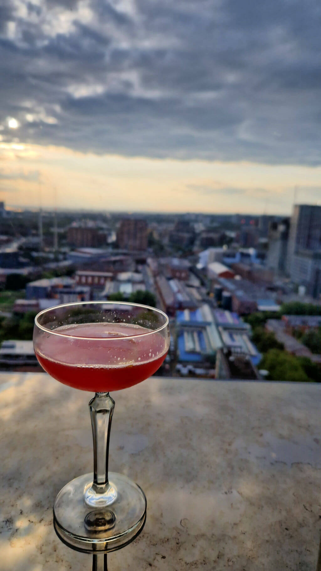 A view across Manchester from the cocktail bar of a tall hotel building.  There is a cocktail in a glass in the foreground