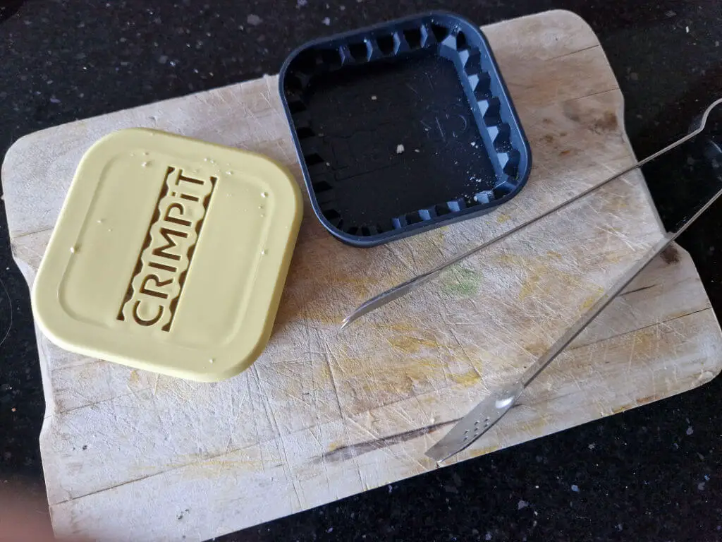 Two halves of a square plastic sandwich press on a wooden chopping board