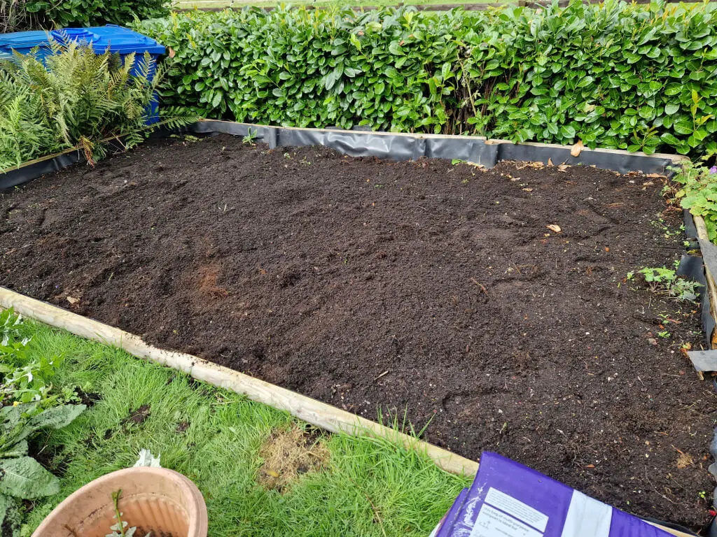 A large empty garden border edged by a wooden frame
