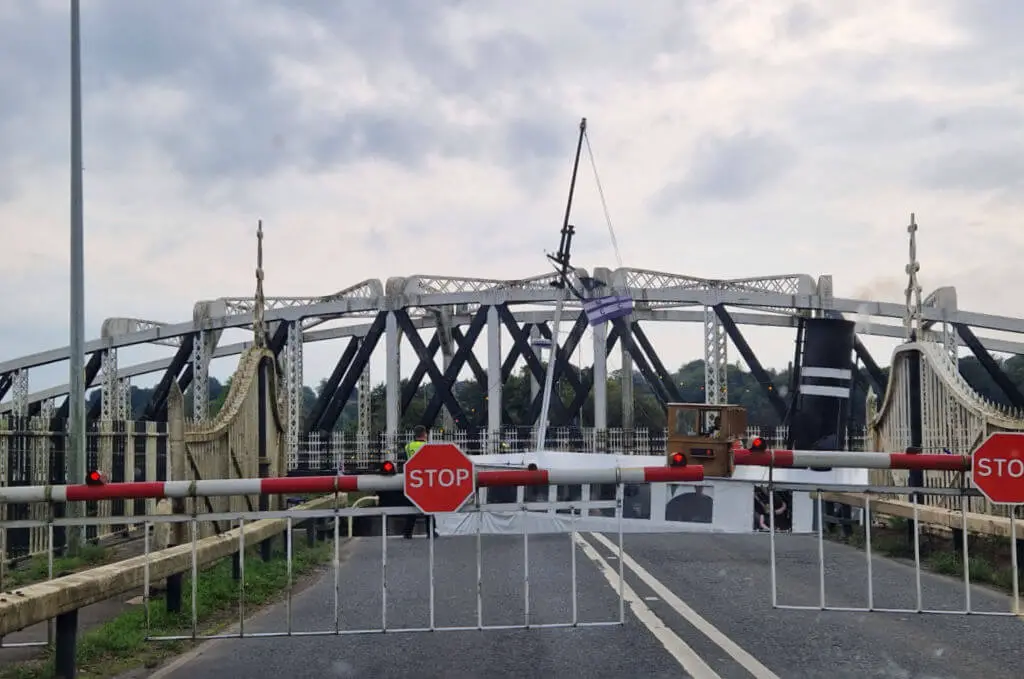 A steam boat sailing through the gap left by a swing bridge 
