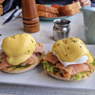 Two poached eggs with hollandaise sauce, smoked salmon and avocado on a rectangular plate on a cafe table
