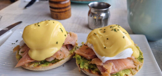 Two poached eggs with hollandaise sauce, smoked salmon and avocado on a rectangular plate on a cafe table