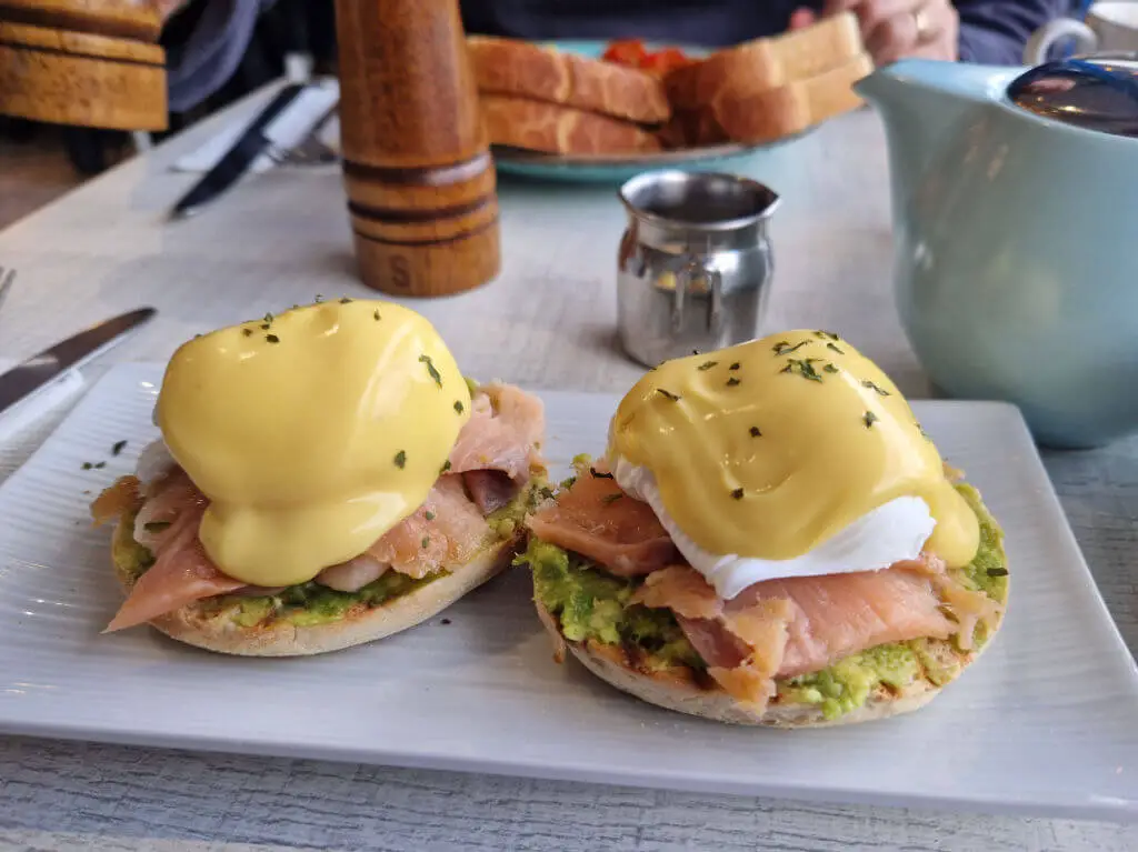 Two poached eggs with hollandaise sauce, smoked salmon and avocado on a rectangular plate on a cafe table