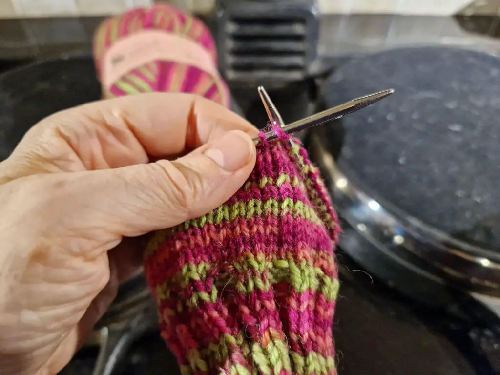 A partly knitted pink and neon green sock on a short circular needle