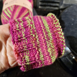 A partly knitted sock held so that you can see the pink and neon green stripes