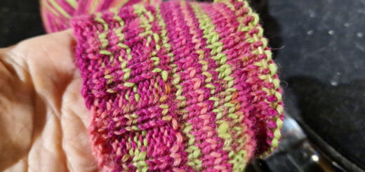 A partly knitted sock held so that you can see the pink and neon green stripes