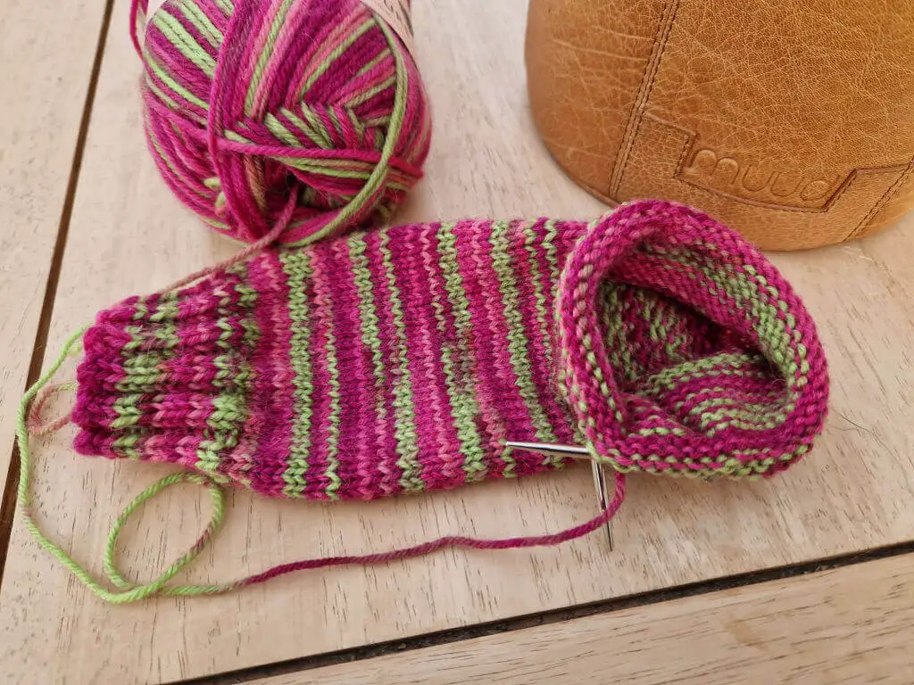 A partly knitted pink and green sock