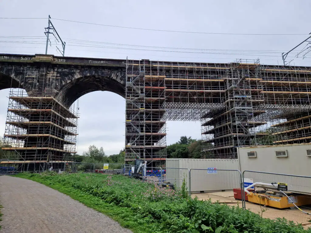 A view of scaffolding on a brick built railway viaduct with container units for the contractors underneath