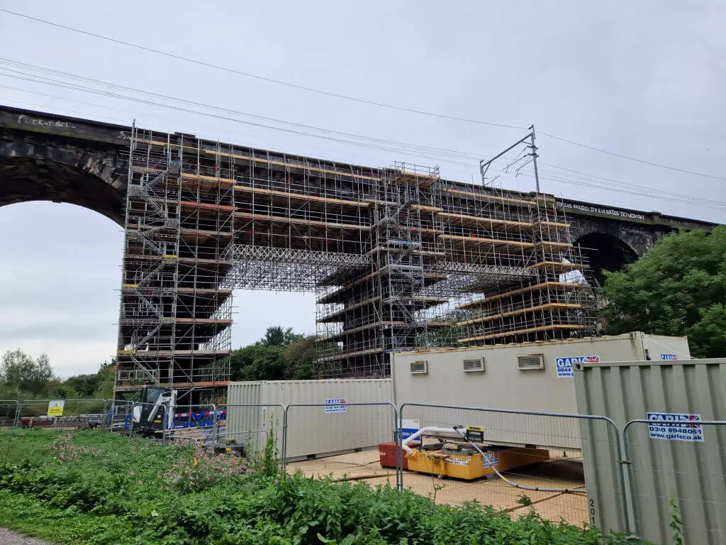 A view of scaffolding on a brick built railway viaduct with container units for the contractors underneath
