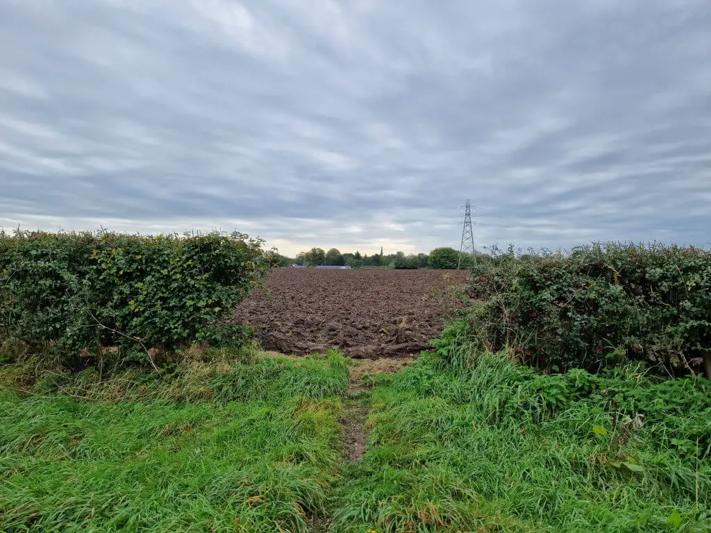 A footpath through hedges is cut off by a ploughed field