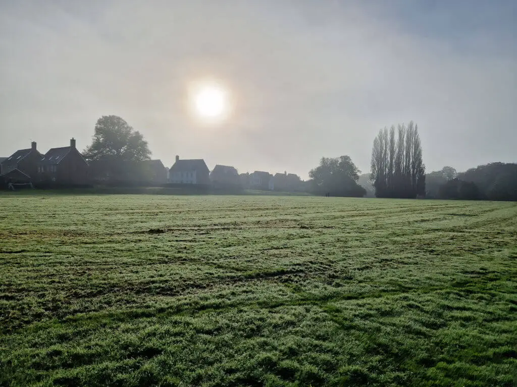 A view across a misty fields where the sun is partly obscured by mist