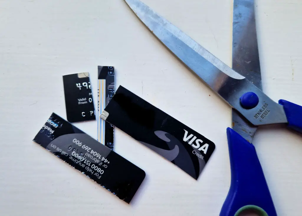 A chopped up credit card lying on a white table next to an open pair of scissors