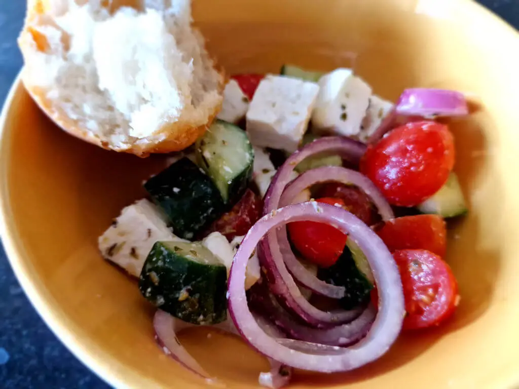 A yellow bowl of Greek salad consisting of cucumber, tomato, red onion and feta cheese