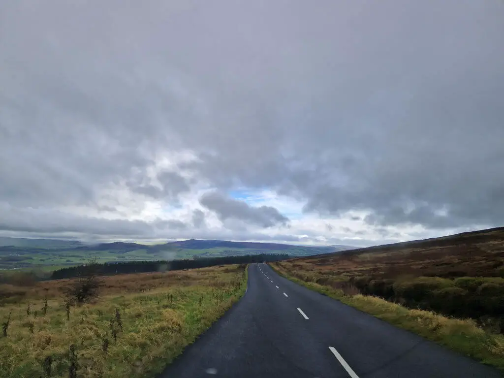 A view along a moorland road. There are grey skies up ahead promising rain