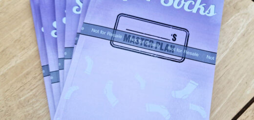 A pile of purple books with the words Project Super Socks printed on them is stacked on a wooden coffee table