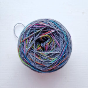 A small cake of rainbow and grey yarn sitting on a white windowsill