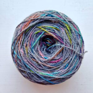 A large cake of rainbow and grey yarn sitting on a white windowsill