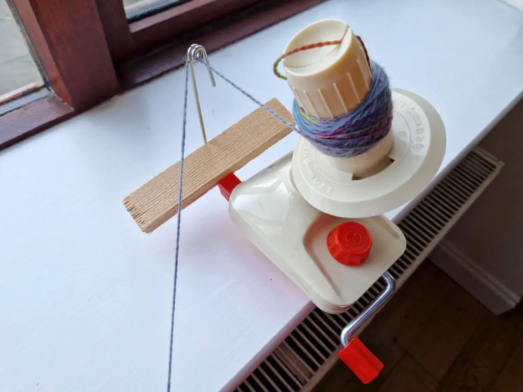 A yarn winder attached to a window sill and wedged with a piece of wood so that the guide doesn't slip