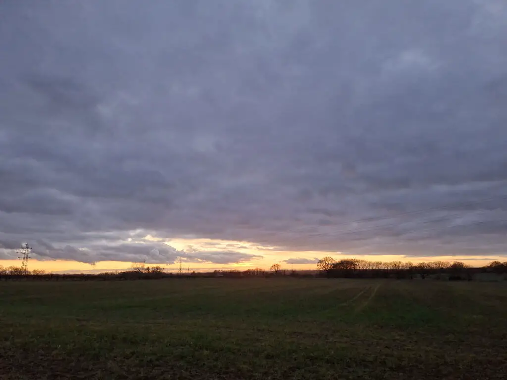 A narrow band of golden sunset sandwiched between dark fields and a dark grey sky
