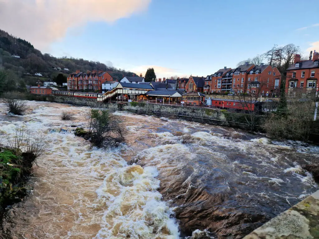 A raging river with a view across to a train station and houses