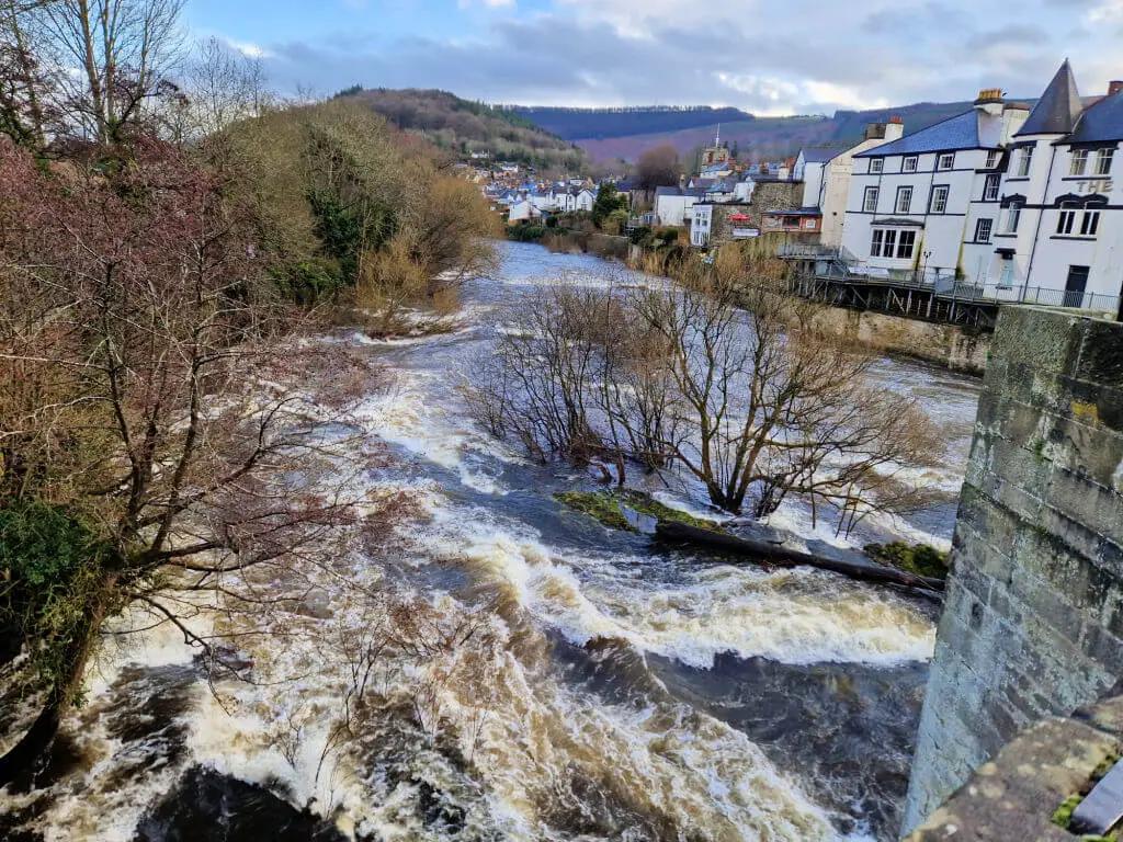 A raging river with a view across to a hotel and hills in the distance