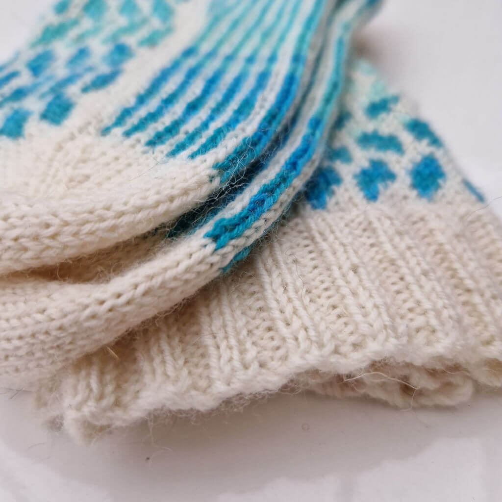 A partial view of a pair of hand knitted socks in cream and blue colourwork