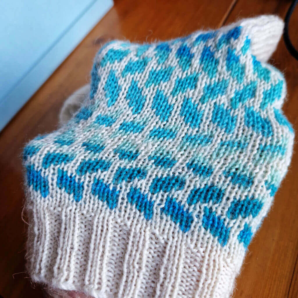 A cream and blue striped colourwork sock stretched over a hand to show that the fabric is still flexible