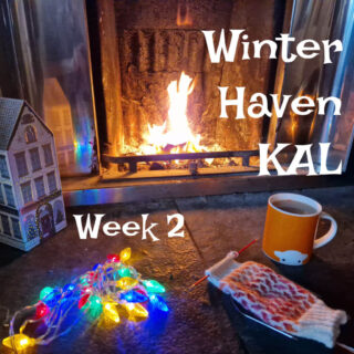 A partly knitted pink, red and cream colourwork sock on a stone hearth next to an open fire