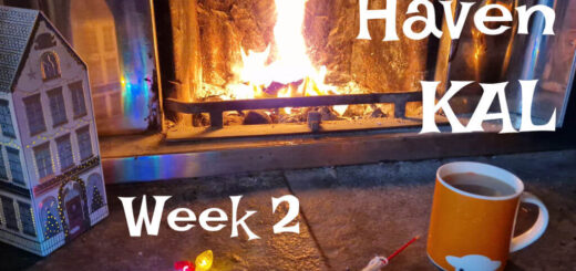 A partly knitted pink, red and cream colourwork sock on a stone hearth next to an open fire
